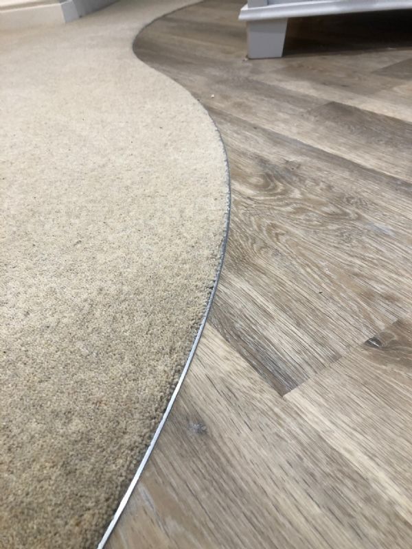Curved threshold Shaun cut between carpet and grey oak-effect plank flooring, finished with a polished trim