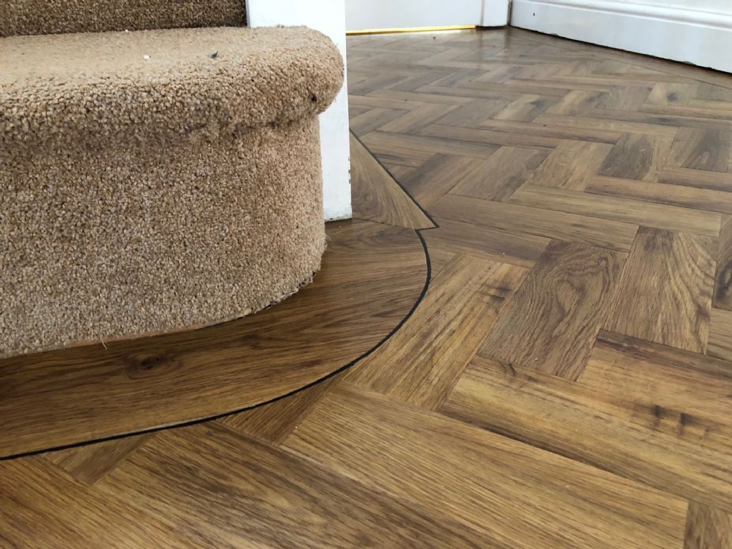 Herringbone luxury vinyl with a curved scribed border, fitted around a carpeted stair